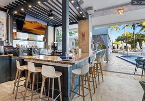A bar area with a poolside view, featuring a bar counter, stools, and a large screen. - Stylish Miami Beach Oceanfront Hilton Hotel Pool Gym WiFi (Miami Beach)