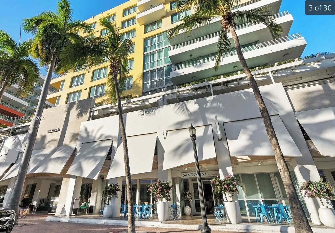 Un hotel de varios pisos con fachada amarilla, palmeras y zonas de estar al aire libre.