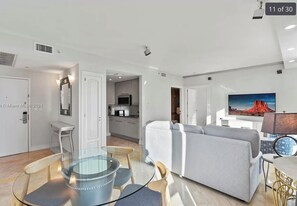 A modern living room with a grey sofa, a glass coffee table, and a TV mounted on the wall. - Stylish Miami Beach Oceanfront Hilton Hotel Pool Gym WiFi (Miami Beach)