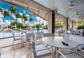 A poolside area with lounge chairs and tables, a swimming pool, and palm trees in the background. - Stylish Miami Beach Oceanfront Hilton Hotel Pool Gym WiFi (Miami Beach)