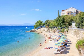 A beach with clear blue waters, a stone wall, and a building with balconies.