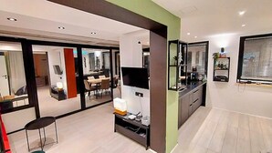 Een moderne hotelkamer met een grote televisie, een zithoek met een tafel en stoelen, en een kitchenette met een spoelbak en aanrecht.