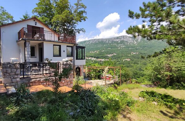 A white villa with a stone facade, a balcony, and a vineyard view.