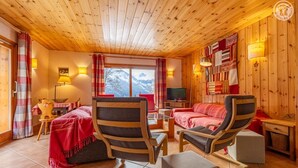 Een gezellige kamer met een bed, twee fauteuils, een bank, een televisie en een raam met uitzicht op de bergen.
