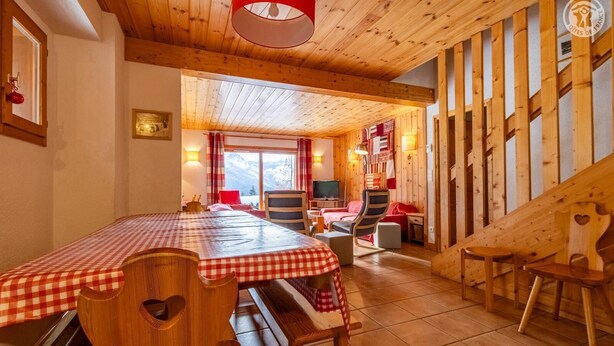Een houten interieur met een tafel met ruitjes, stoelen, een bed en een televisie.