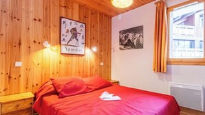 Een kamer met houten lambrisering, een bed, een ingelijst beeld, een raam met gordijnen en een wandlamp.