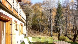Eine Holzhütte mit Balkon, Picknicktisch und zwei Liegestühlen inmitten eines Waldes.