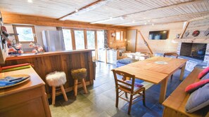 Un interno accogliente di una baita, con un tavolo e sedie in legno, un angolo cottura con frigorifero e un camino.