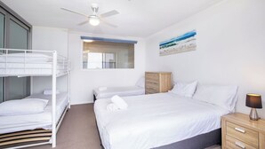 A hotel room with a bunk bed, a single bed, a ceiling fan, a nightstand with a lamp, a wooden cabinet, and a painting of a beach scene. - Stunning Ocean Views from Every Room 
24th level 
Fully Aircond Cental location! (Surfers Paradise)