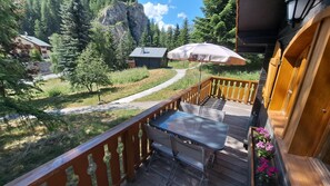 A wooden deck with a table and chairs, overlooking a mountain path and greenery.