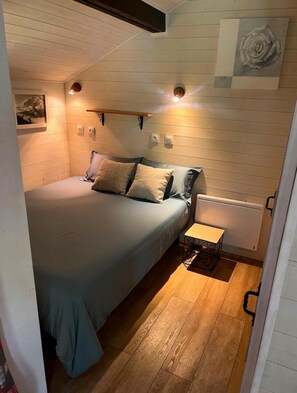 A small, cozy bedroom with a single bed, a bedside table, a radiator, and a wall-mounted light fixture.