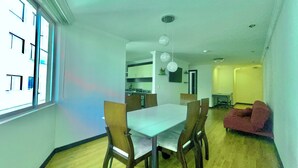 A dining area with a white table and wooden chairs, a kitchen in the background, and a red sofa in the living area. - Torre Bossano (Quito)