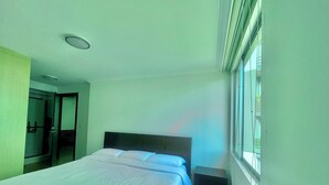 A modern hotel room with a large bed, a small bedside table, a nightstand, and a window with blinds. - Torre Bossano (Quito)