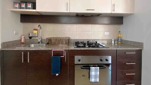 A kitchen with dark wooden cabinets, a stainless steel range hood, a built-in oven, and a granite countertop. - Torre Bossano (Quito)