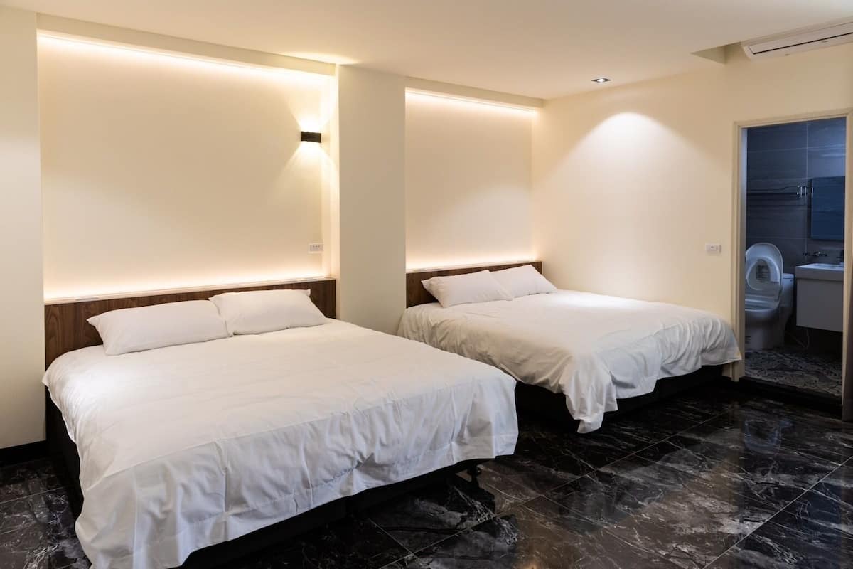 Habitación de hotel con dos camas, baño con inodoro y lavamanos, y piso de mármol.
