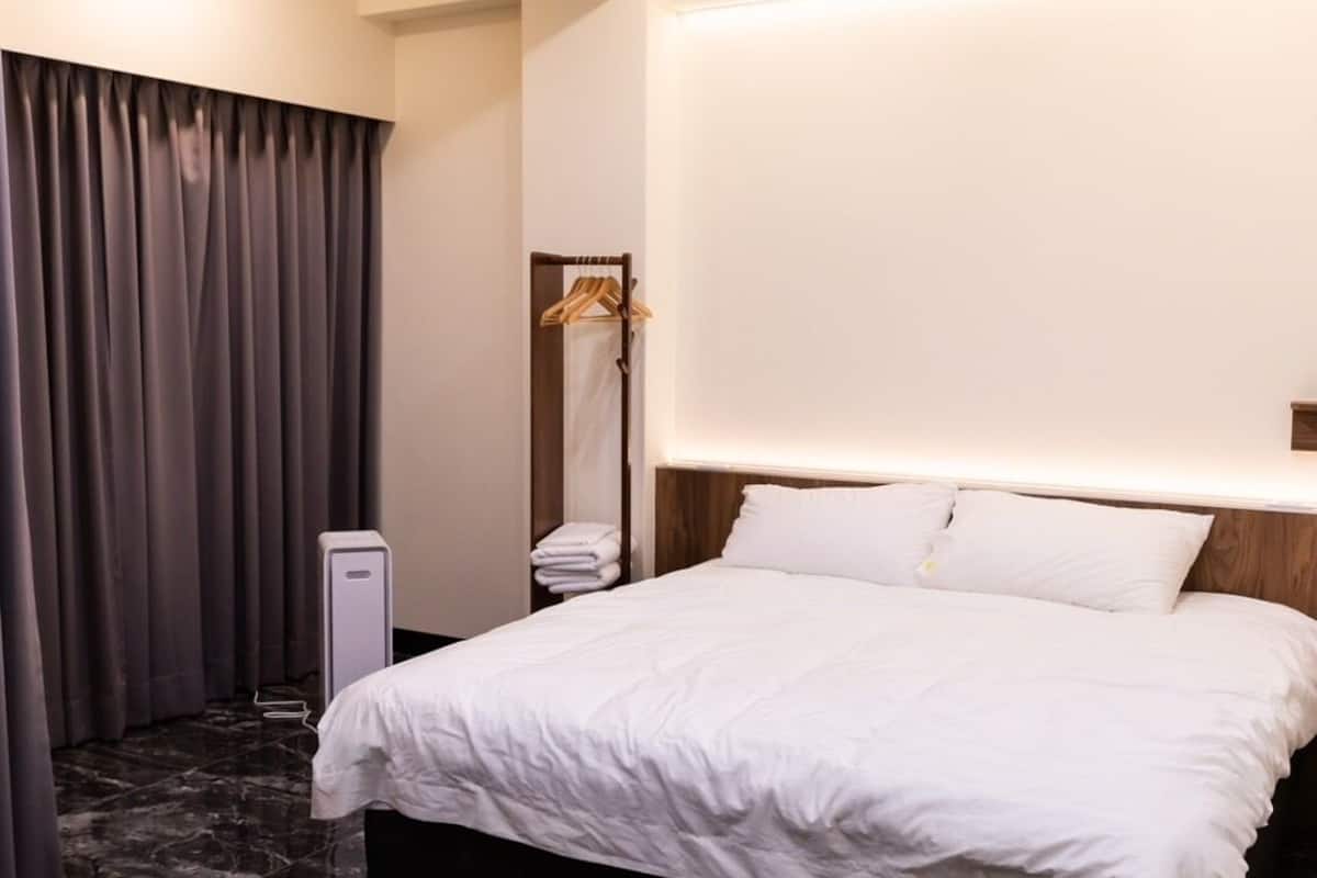 Una habitación de hotel moderna con una cama grande, suelo de mármol oscuro y una lámpara fijada a la pared.