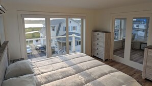 Ein Schlafzimmer mit einem großen Bett, einem Schminktisch und Blick auf ein Haus und Wasser durch das Fenster.