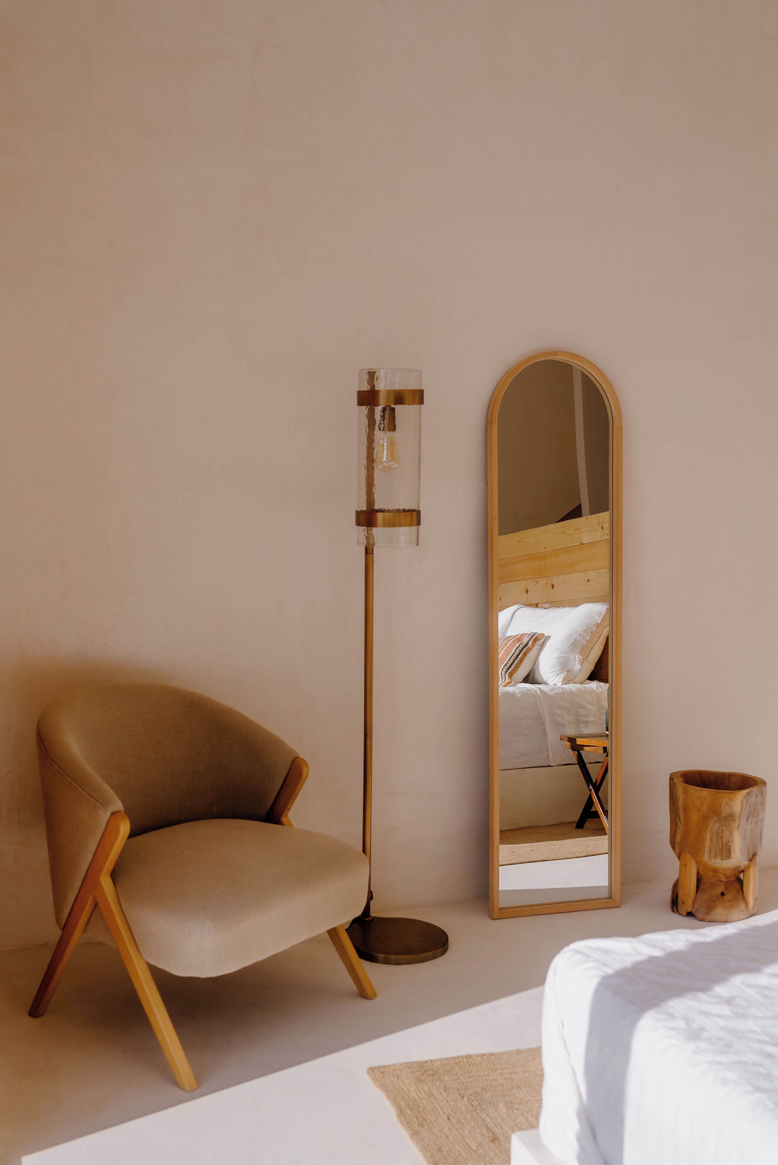 Ein Schlafzimmer mit einem hölzernen Bett, einem beigen Sessel, einer Stehlampe und einem Spiegel, der das Bett widerspiegelt.