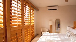 Un dormitorio con cama, una silla, un espejo y una ventana con persianas de madera.