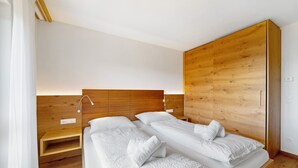 Un dormitorio moderno con cabecera de madera, dos camas con ropa de cama blanca, una mesita de noche y un armario empotrado.