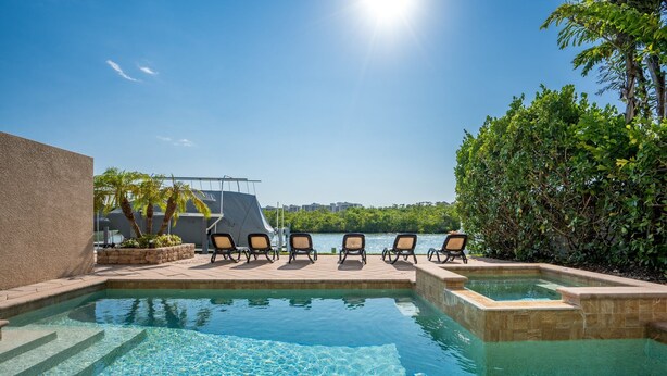 A pool area with clear water, sun loungers, and a view of the water. - MarcoWaterfront-BalconyViews-Pool+Spa-Fishing (Marco Island)
