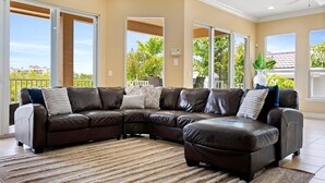 A spacious living room with a large L-shaped sectional sofa, a neutral-toned rug, and a view of a balcony with outdoor furniture. - MarcoWaterfront-BalconyViews-Pool+Spa-Fishing (Marco Island)