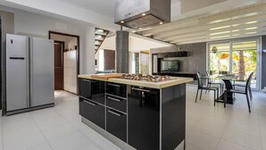 A modern kitchen with a central island, built-in appliances, and a dining area with a glass table and chairs. - Villa 'Green Garden' with Private Terrace, Wi-Fi and Air Conditioning (Carlentini)