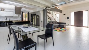 A modern kitchen with white cabinets, a dining table with chairs, a staircase, and a living area with a sofa. - Villa 'Green Garden' with Private Terrace, Wi-Fi and Air Conditioning (Carlentini)