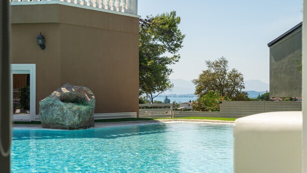 A swimming pool with a large rock, a building with a white door, and a view of mountains in the background. - Holiday Home 'Villa Leon with Private Pool' with Sea View, Wi-Fi and Air Conditioning (Quartu Sant'Elena)