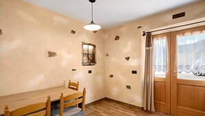 Una habitación con una mesa de comedor de madera, sillas, una ventana con vistas y una puerta con cortinas.