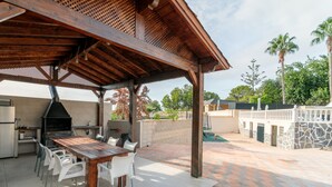 Eine Terrasse im Freien mit einem Holztisch und -stühlen, einem Grill und einer Steinmauer.