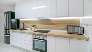 Eine moderne Küche mit weißen Schränken, einem Edelstahlkühlschrank, einem eingebauten Backofen und einer Mikrowelle.