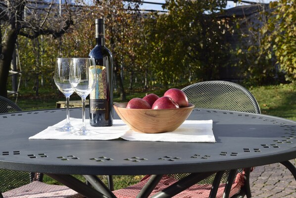 A round metal table with a bottle of wine, two glasses, and a bowl of red apples.