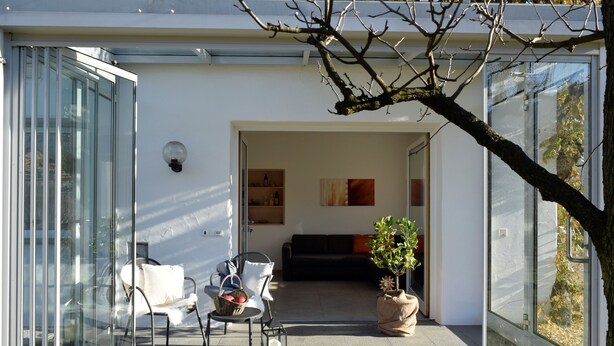 A modern interior with a glass door leading to a living area, a sofa, a coffee table, and a potted plant.