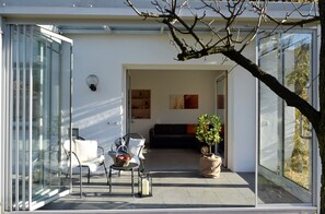 Un interior moderno con un vidrio que da a un salón, un sofá, una mesa de centro y una planta en maceta.