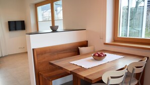 A dining area with a wooden table, white chairs, and a bowl of fruit.
