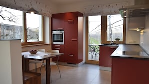 A modern kitchen with red cabinetry, a dining area with a table and chairs, and a view of the outdoors through large windows.
