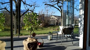A glass-enclosed patio with a view of a grassy area and trees, a wicker basket with apples, and a metal chair.