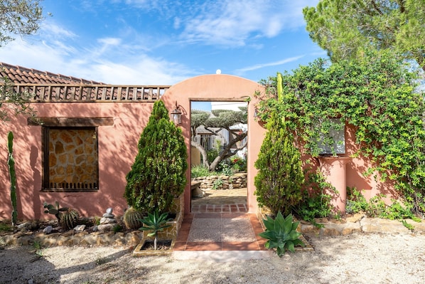 Un bâtiment doté d’un toit en tuiles, d’une fenêtre encadrée de pierres et d’une porte donnant sur un jardin.