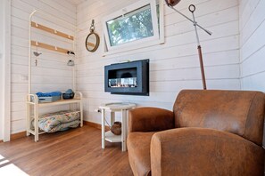 Et værelse med en brun lædersofa, en hvid metalkasse med vasketøj, et lille hvidt bord med en vase, en pejs og et vindue med udsigt til træer.