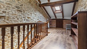 Une pièce avec un mur en pierre, des poutres en bois, un escalier en bois et un mur en briques.