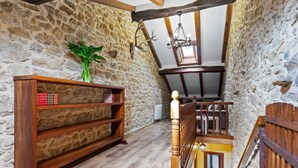 Une pièce aux murs de pierre, avec une bibliothèque en bois, un escalier et un luminaire suspendu.