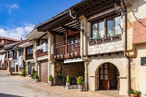 Une rangée de bâtiments traditionnels en pierre, dotés de balcons et de plantes en pot, sous un ciel d’un bleu éclatant.