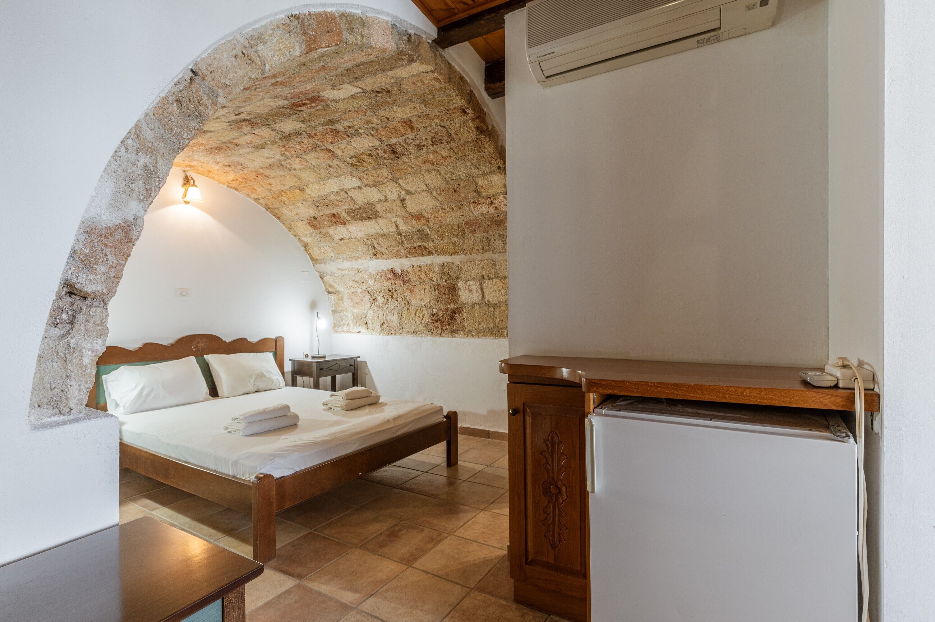 Un dormitorio con un arco de piedra, una cama, un aparador de madera y una mesita.