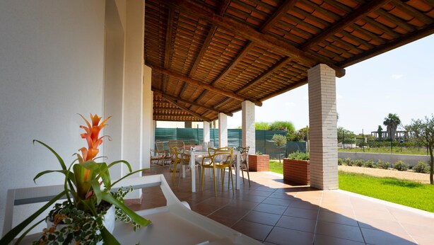 A covered patio area with a dining table and chairs, a potted plant, and a view of a green landscape. - Holiday Home 'Suite La Barracca' with Sea View, Wi-Fi and Air Conditioning (Marsala)