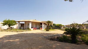 A house with a covered patio, a gravel driveway, and a small garden with a palm tree. - Holiday Home 'Suite La Barracca' with Sea View, Wi-Fi and Air Conditioning (Marsala)