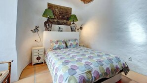 A bedroom with a bed, a nightstand, a lamp, and a wall-mounted shelf with decorative items. - Vacation Home 'Palacio Taro Chimida' with Private Pool (Teguise)
