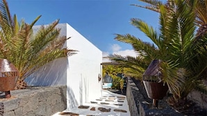 A pathway leading to a building with a white facade, palm trees, and a stone wall. - Vacation Home 'Palacio Taro Chimida' with Private Pool (Teguise)