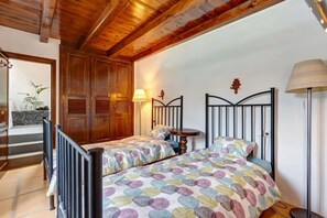 A bedroom with two beds, wooden wardrobe, a lamp, and a staircase.