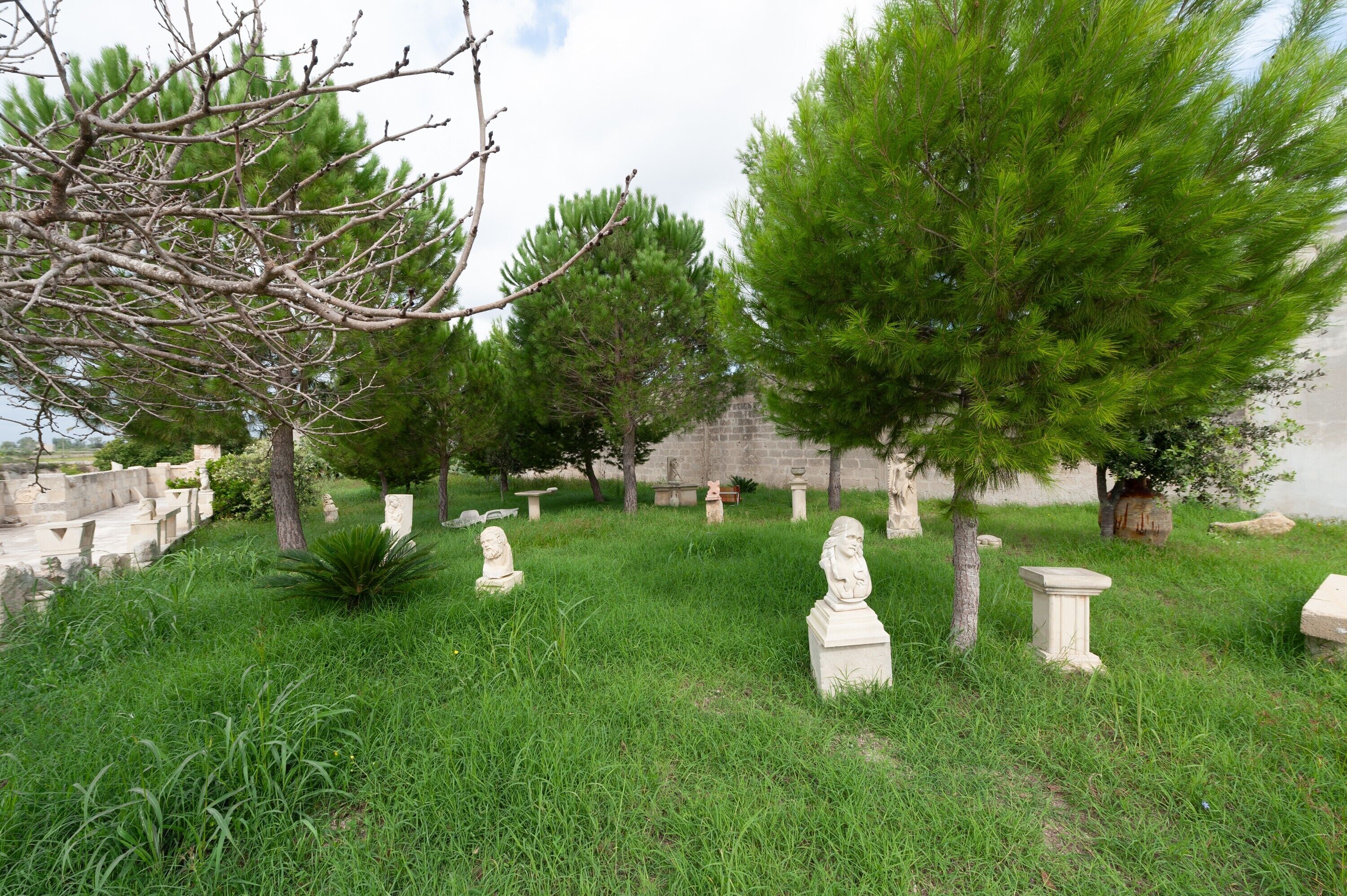 A cemetery with stone statues, trees, and a stone wall.